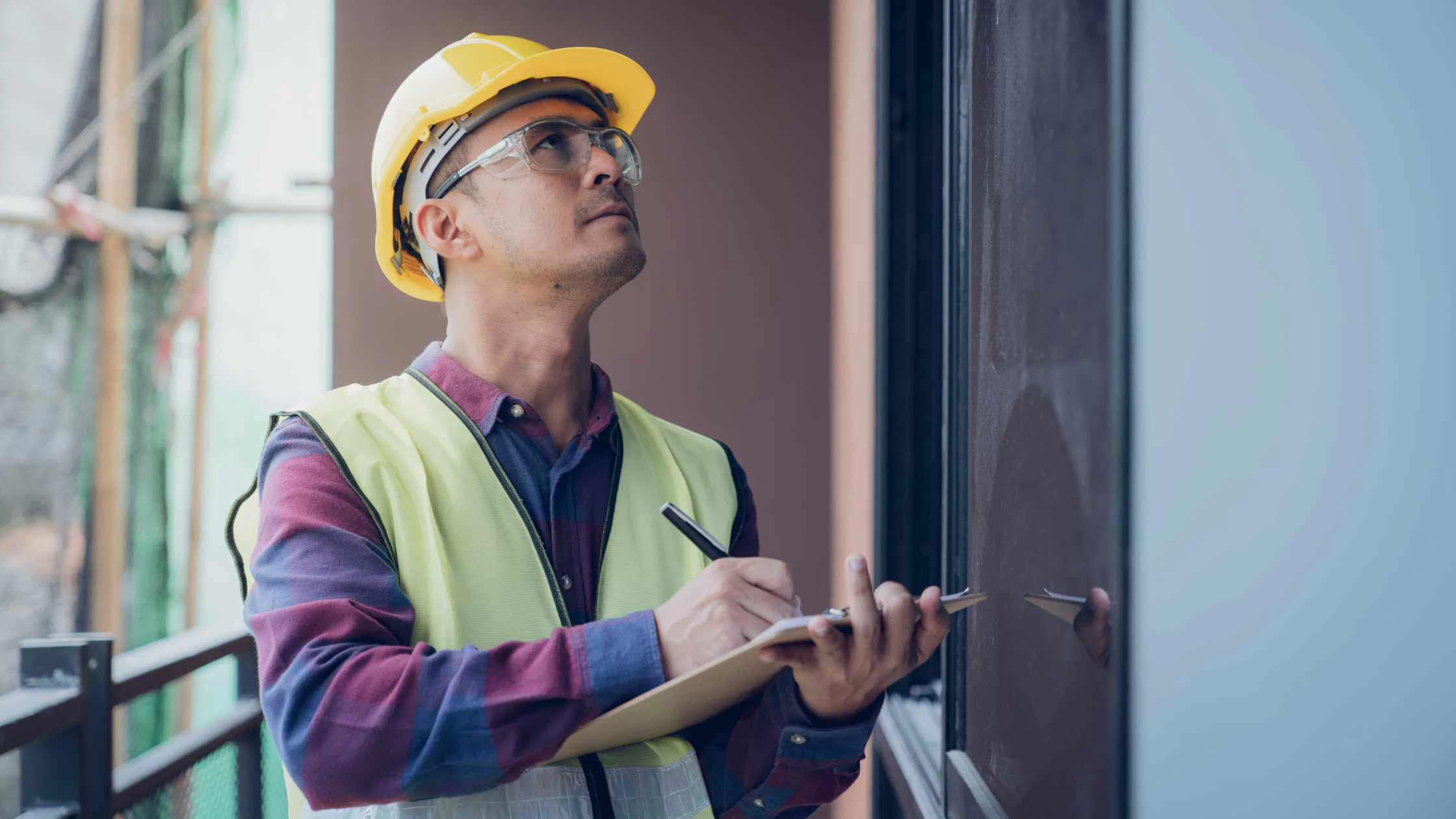 Construction worker inspecting building, clipboard in hand.