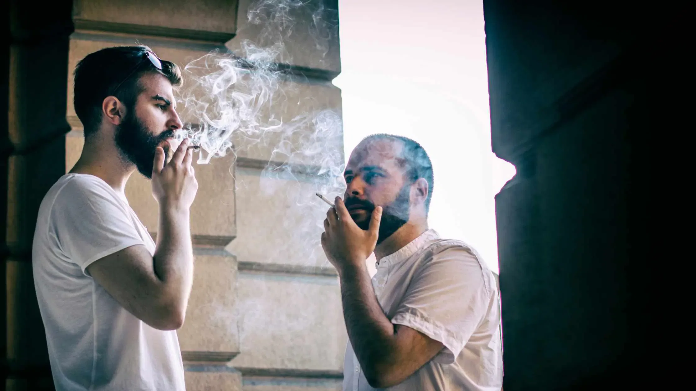 Two men smoking cigarettes outside a building.