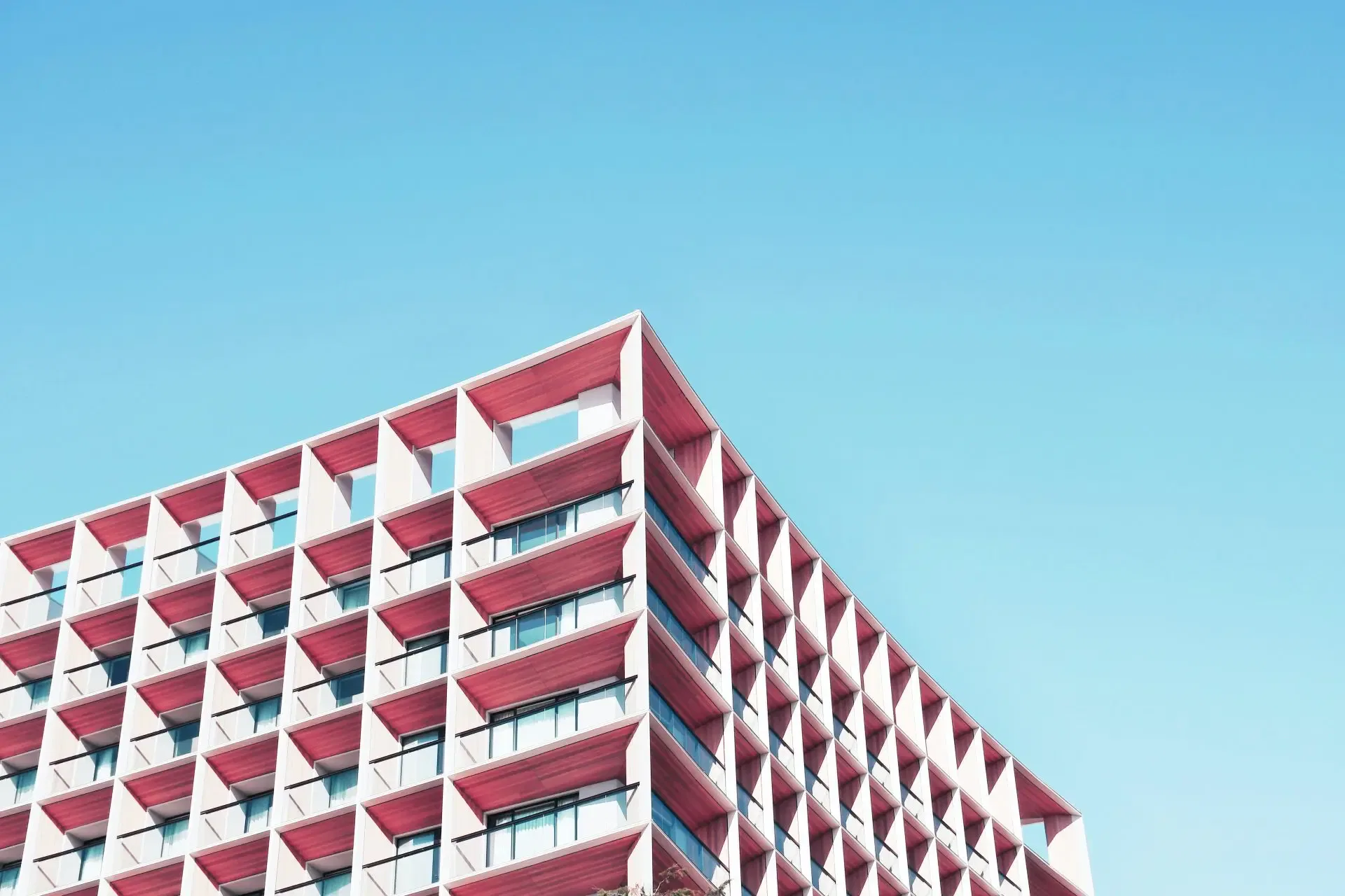 Modern building with red geometric balconies against a clear blue sky, viewed from an upward angle.