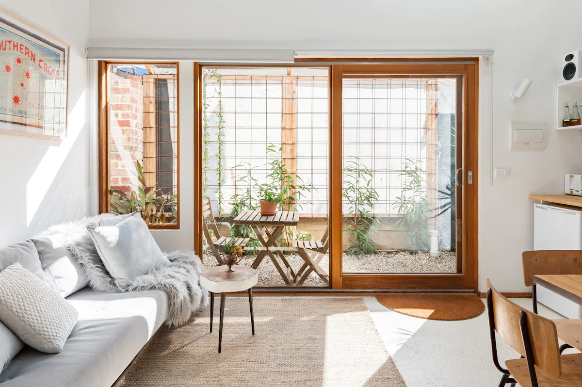 Cozy living room with a gray couch, accent pillows, a small wooden table, and large sliding glass doors leading to a small garden patio.