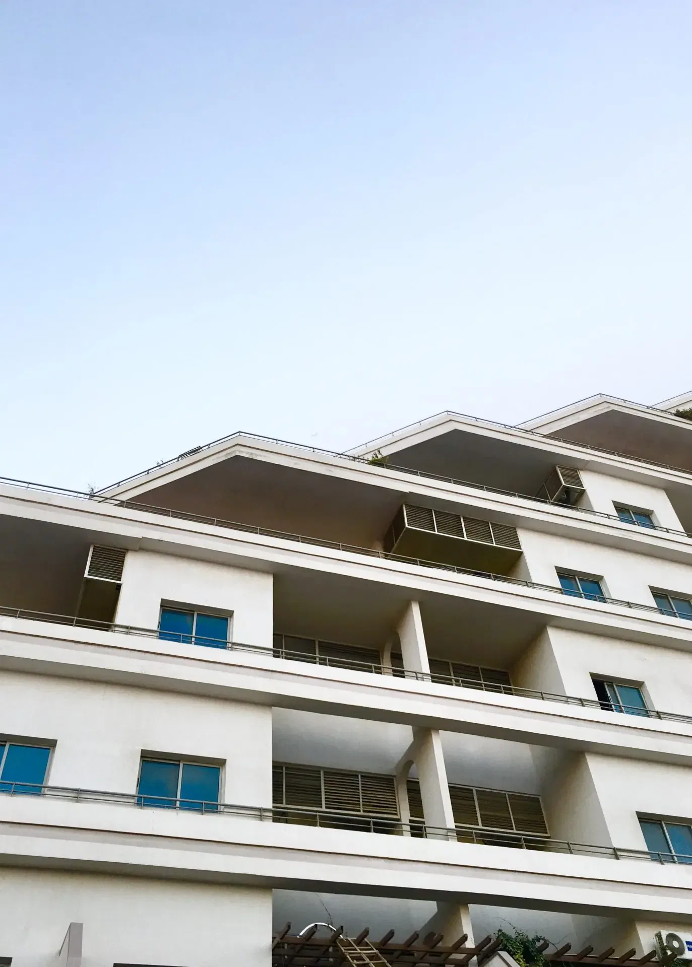 Modern apartment building with multiple balconies and a clean white exterior under a clear blue sky.