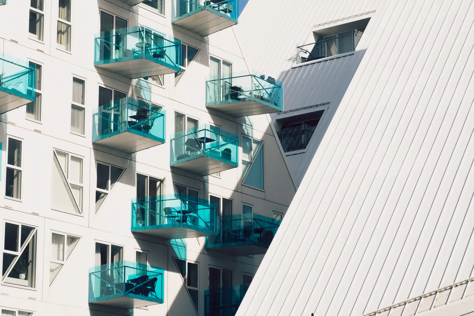 Modern building with white facade and multiple blue glass balconies, featuring slanted architectural designs and large windows.