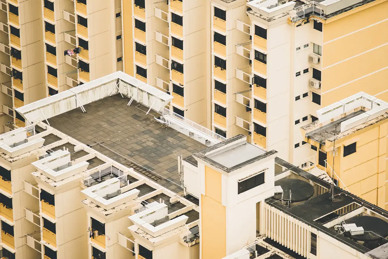 Aerial view of a beige and yellow high-rise residential building with a large rooftop area, featuring multiple balconies.
