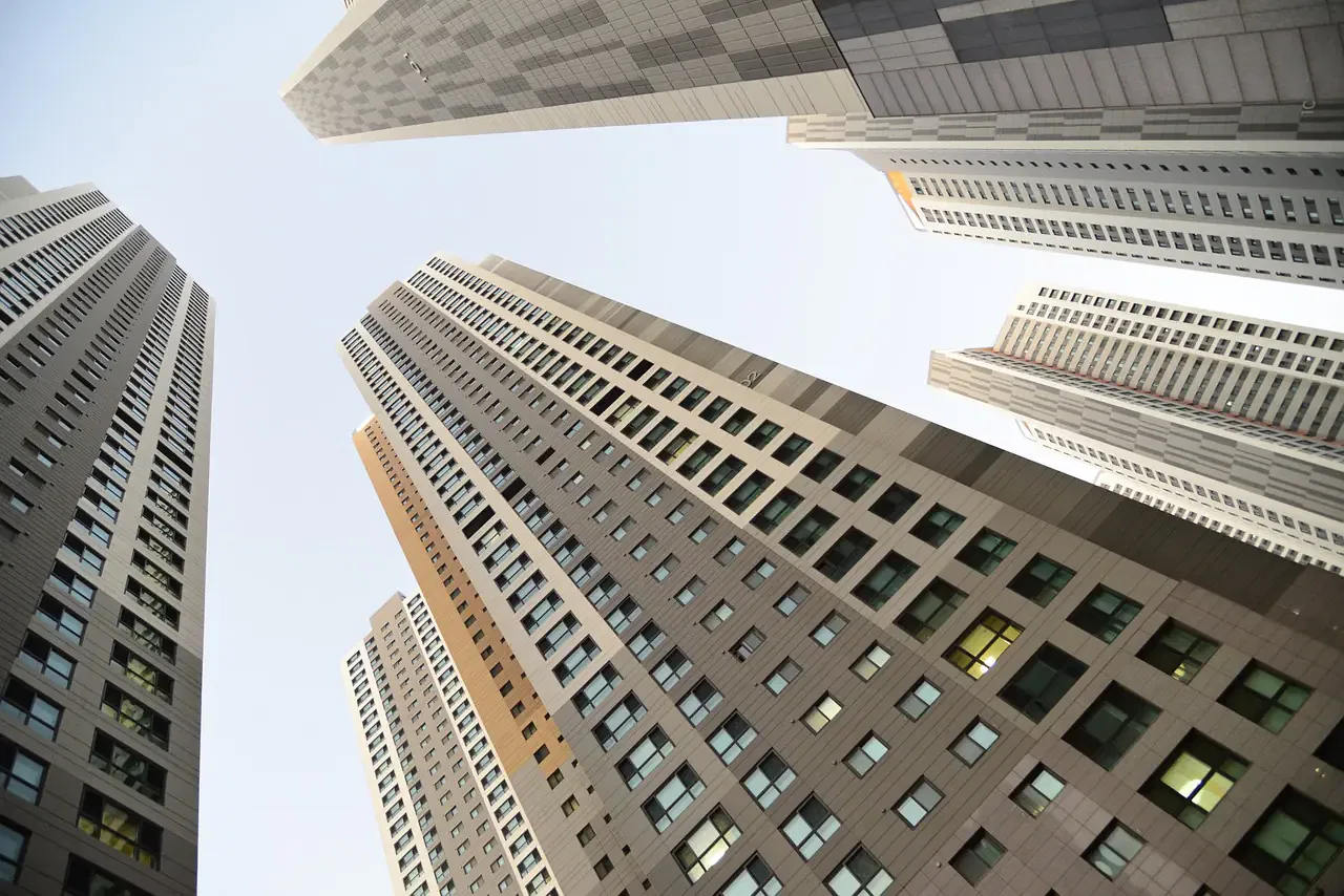 Upward view of several tall skyscrapers under a clear sky, showcasing modern architecture with numerous windows.