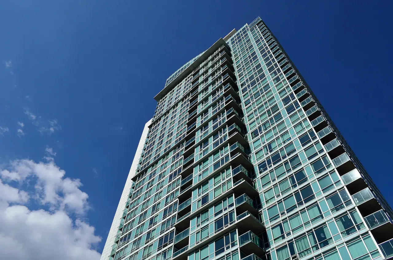 Tall modern glass skyscraper viewed from below against a clear blue sky with a few clouds.