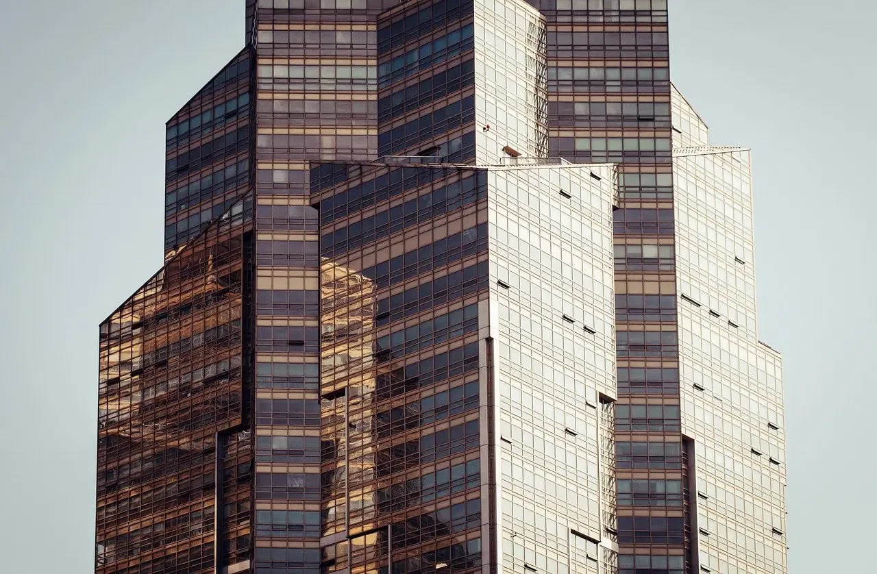 Modern skyscraper with geometric, reflective glass facade under a clear sky. Building shows angular design with multiple tiers.