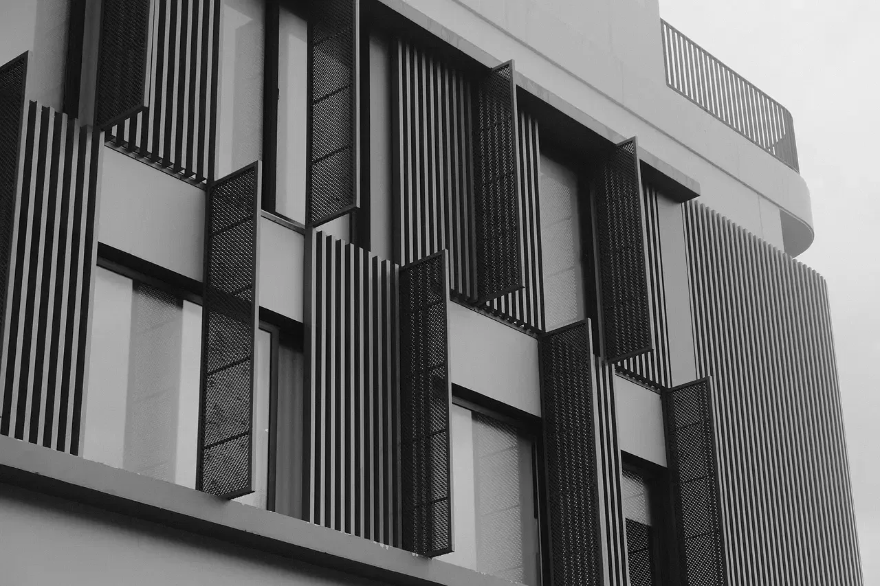 Black and white photo of a modern building facade with vertical slats and grid-patterned window shades.