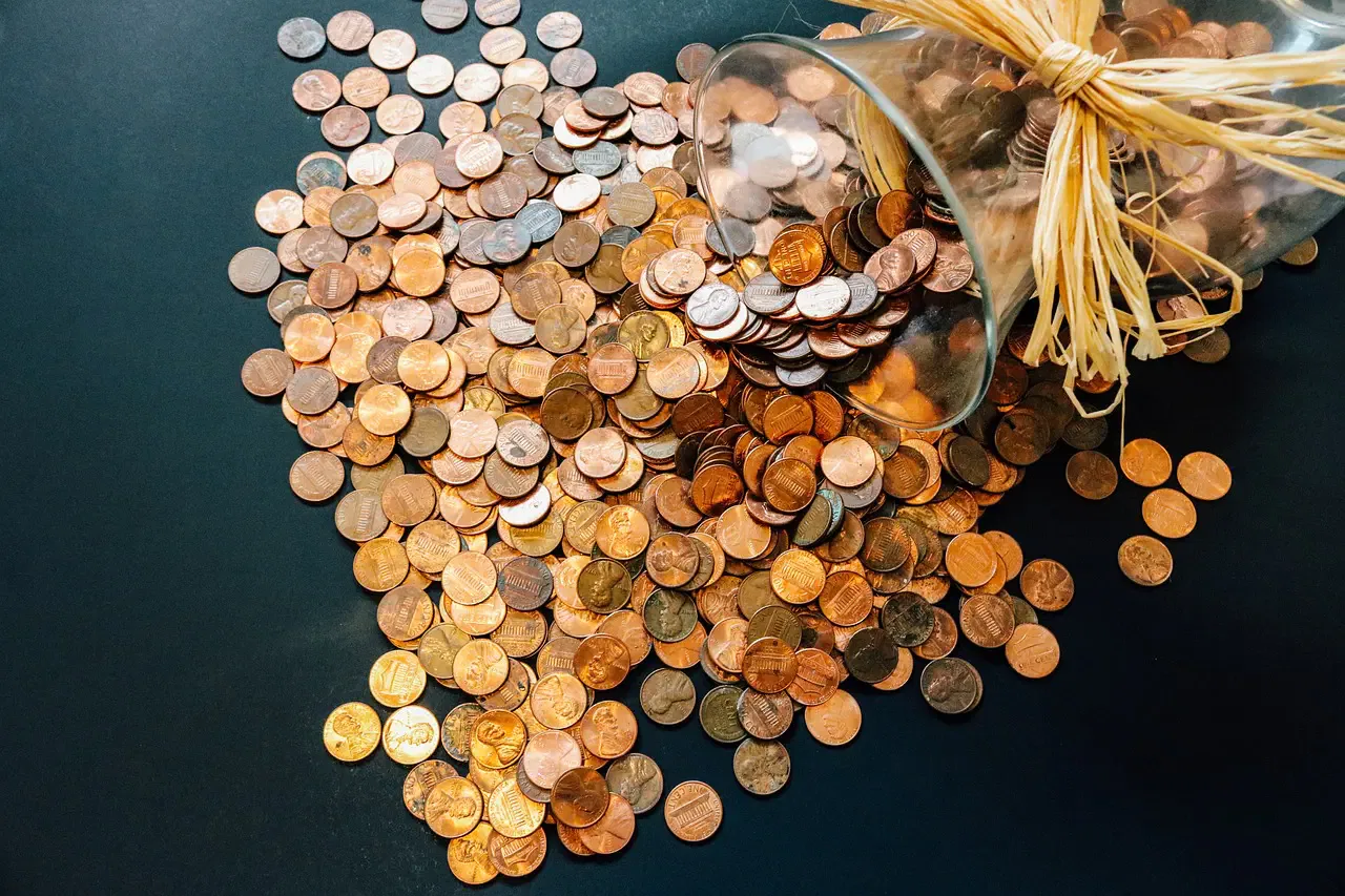 A glass jar tipped over with pennies spilling out onto a dark surface.