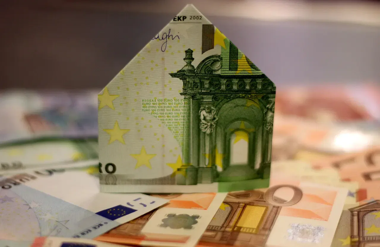 Origami house made from a 100 euro banknote, surrounded by various other euro currency notes.