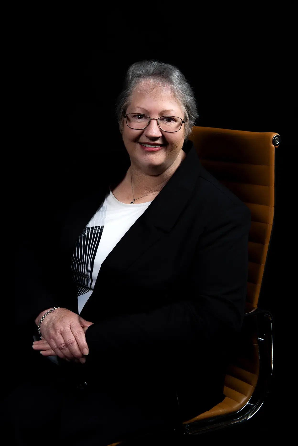 Smiling businesswoman in a black suit sits in an office chair.