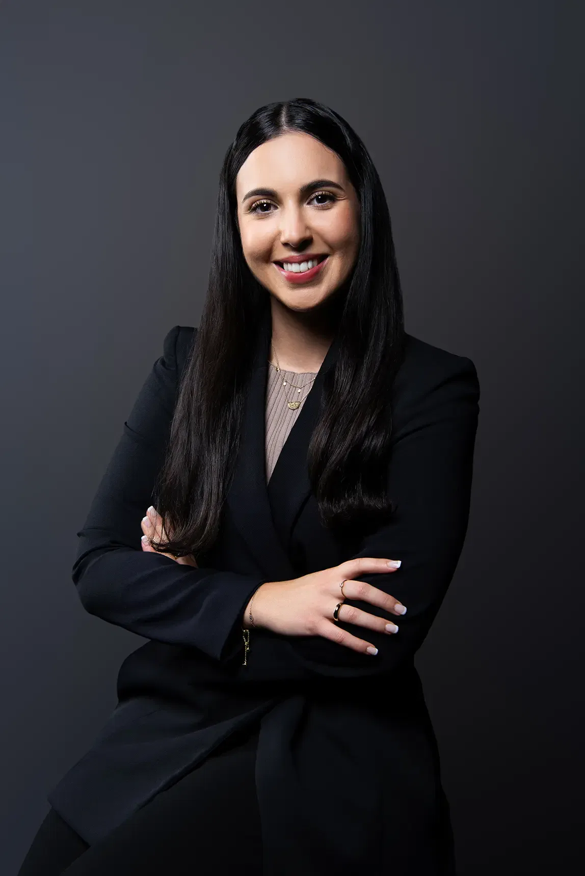 Smiling businesswoman with arms crossed, wearing a black blazer.