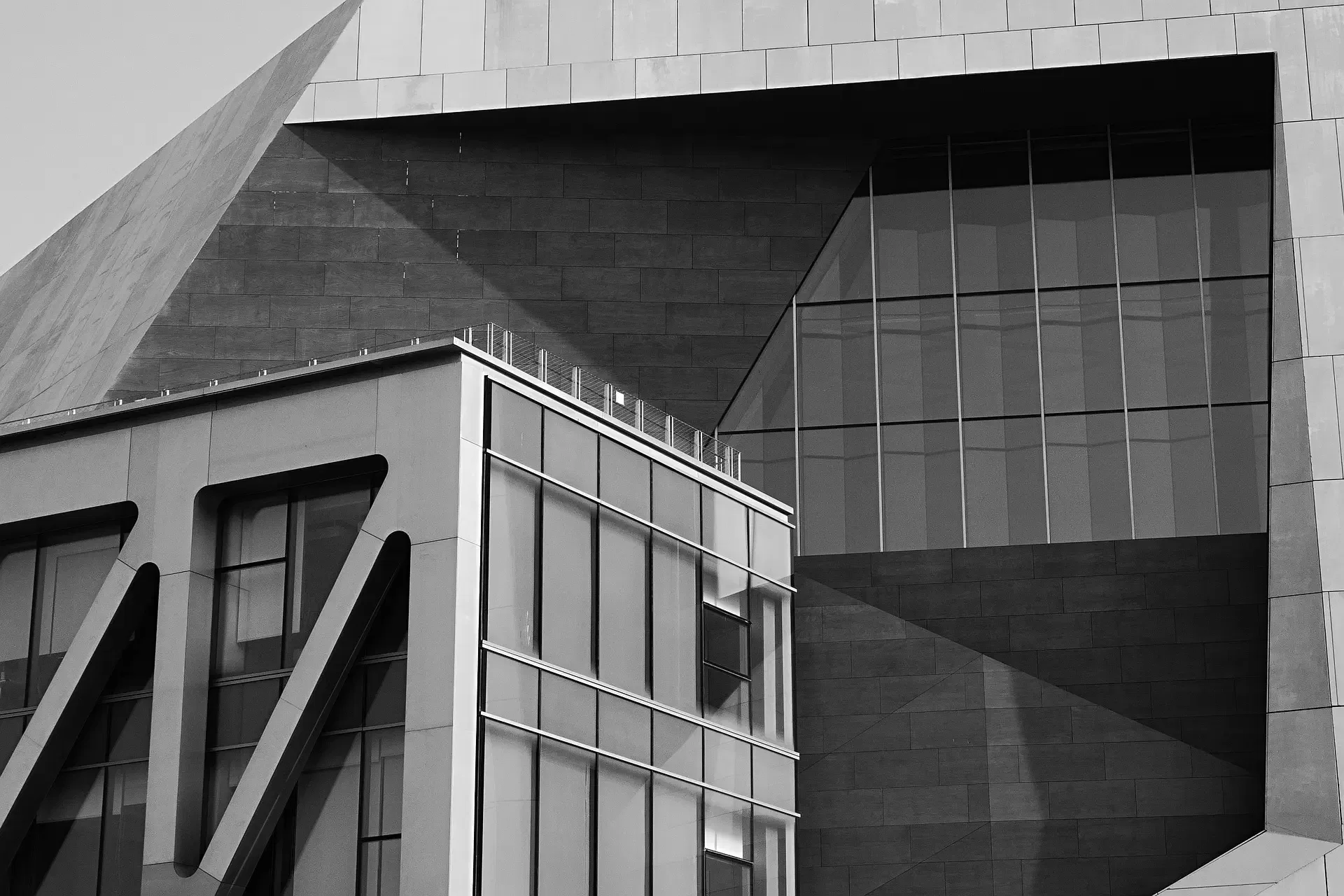 Modern building with angular, geometric design featuring large windows and steel support beams, captured in black and white.