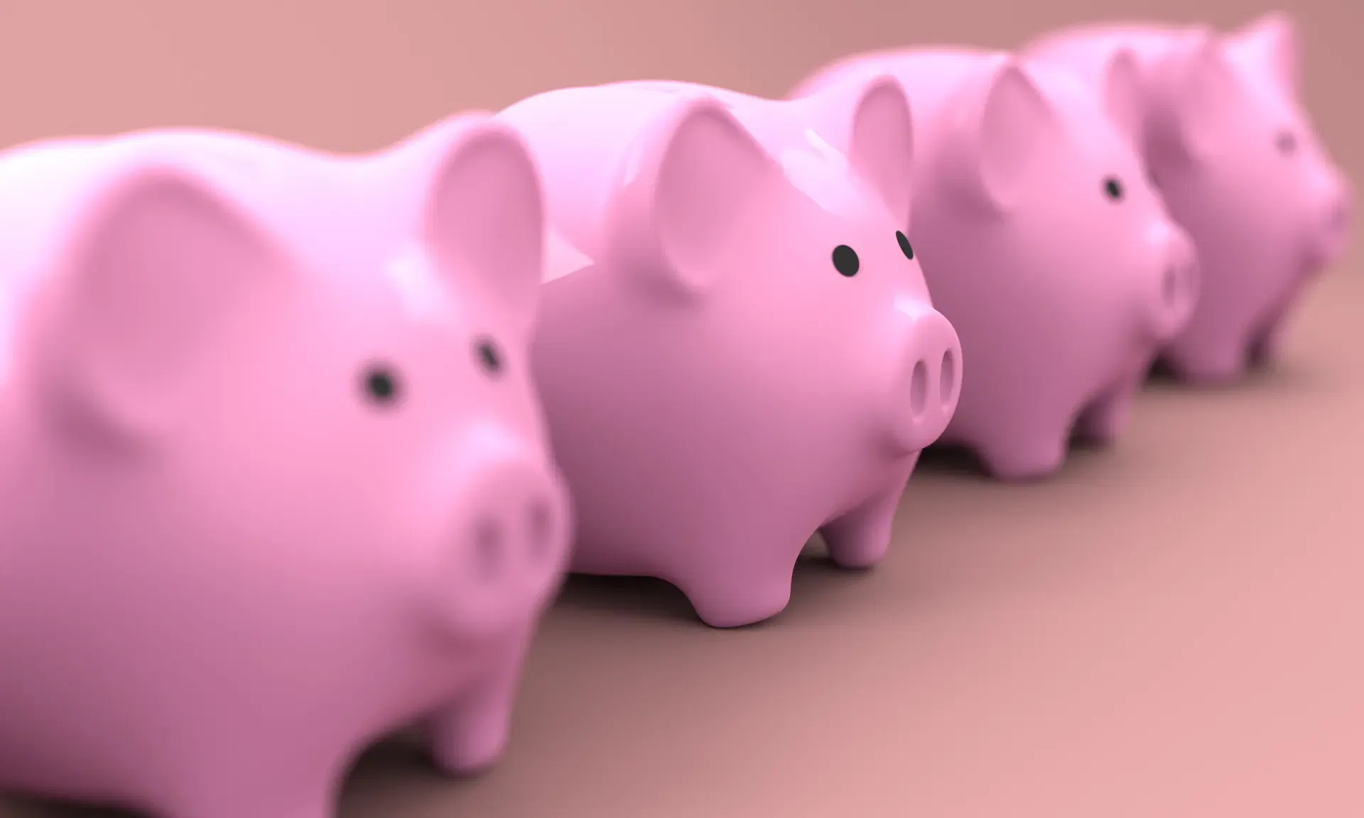 Four pink piggy banks arranged in a row on a soft pink background.
