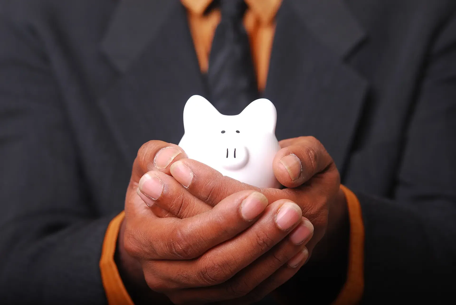 Person in a suit holds a small white piggy bank with both hands, emphasizing financial savings and security.