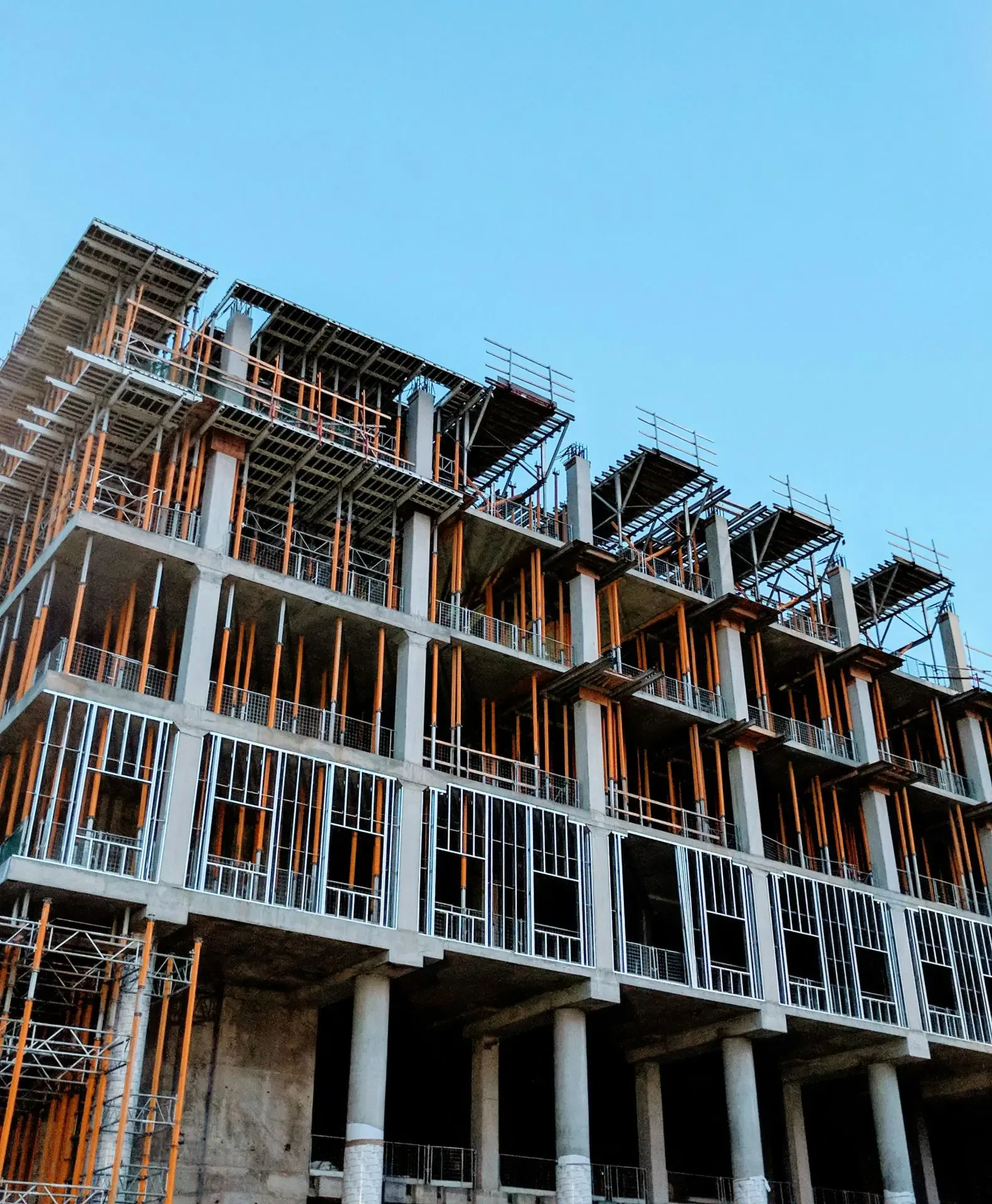 Partially constructed multi-story building with exposed frameworks and scaffolding against a clear blue sky.