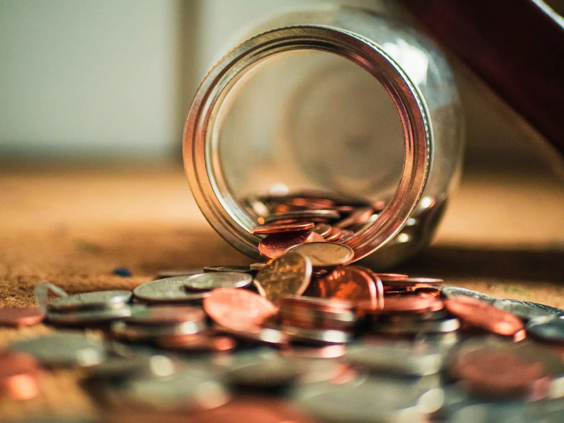Spilled jar with assorted coins scattered on a surface, including copper and silver ones.