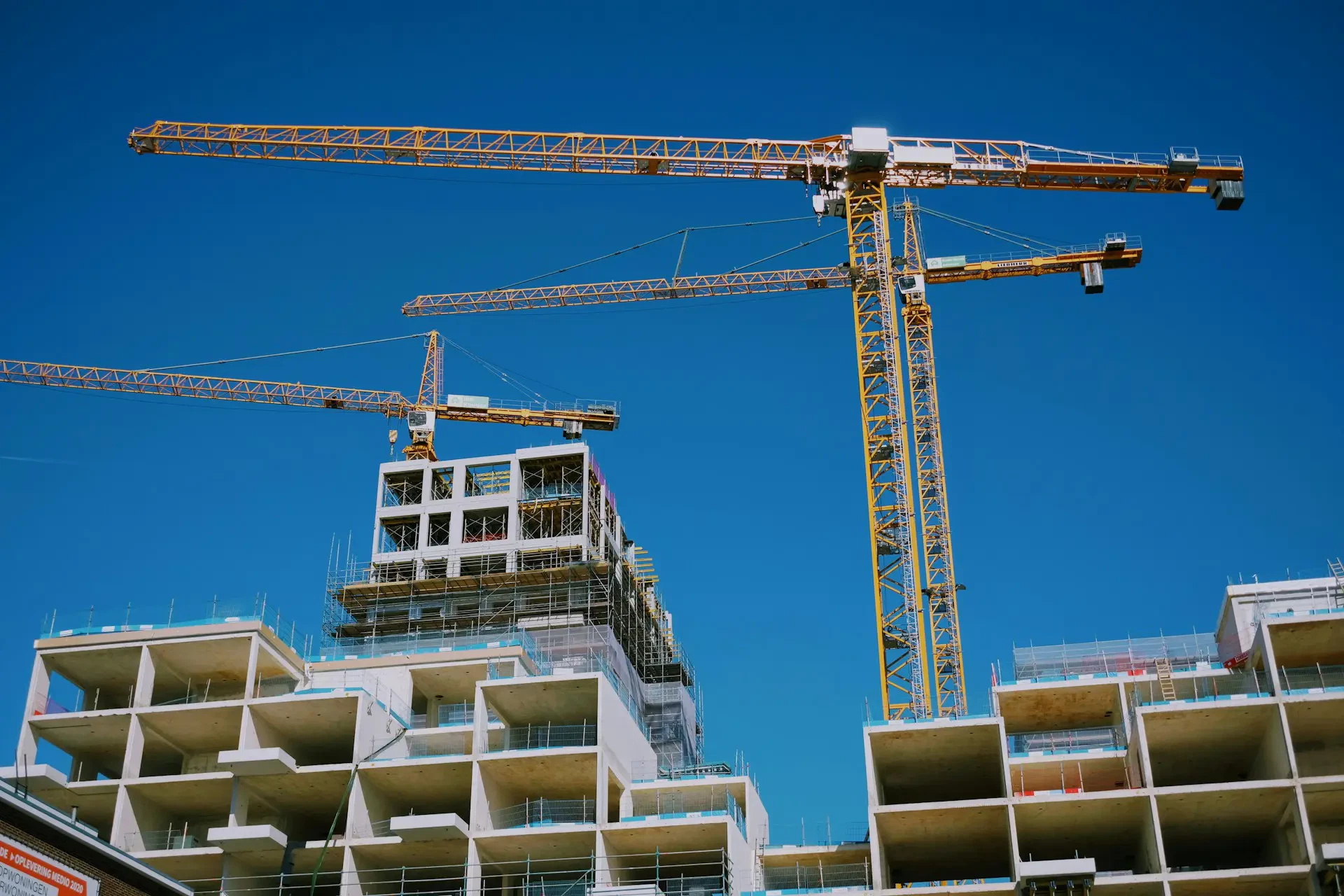 Construction site with cranes and unfinished buildings against a clear blue sky.