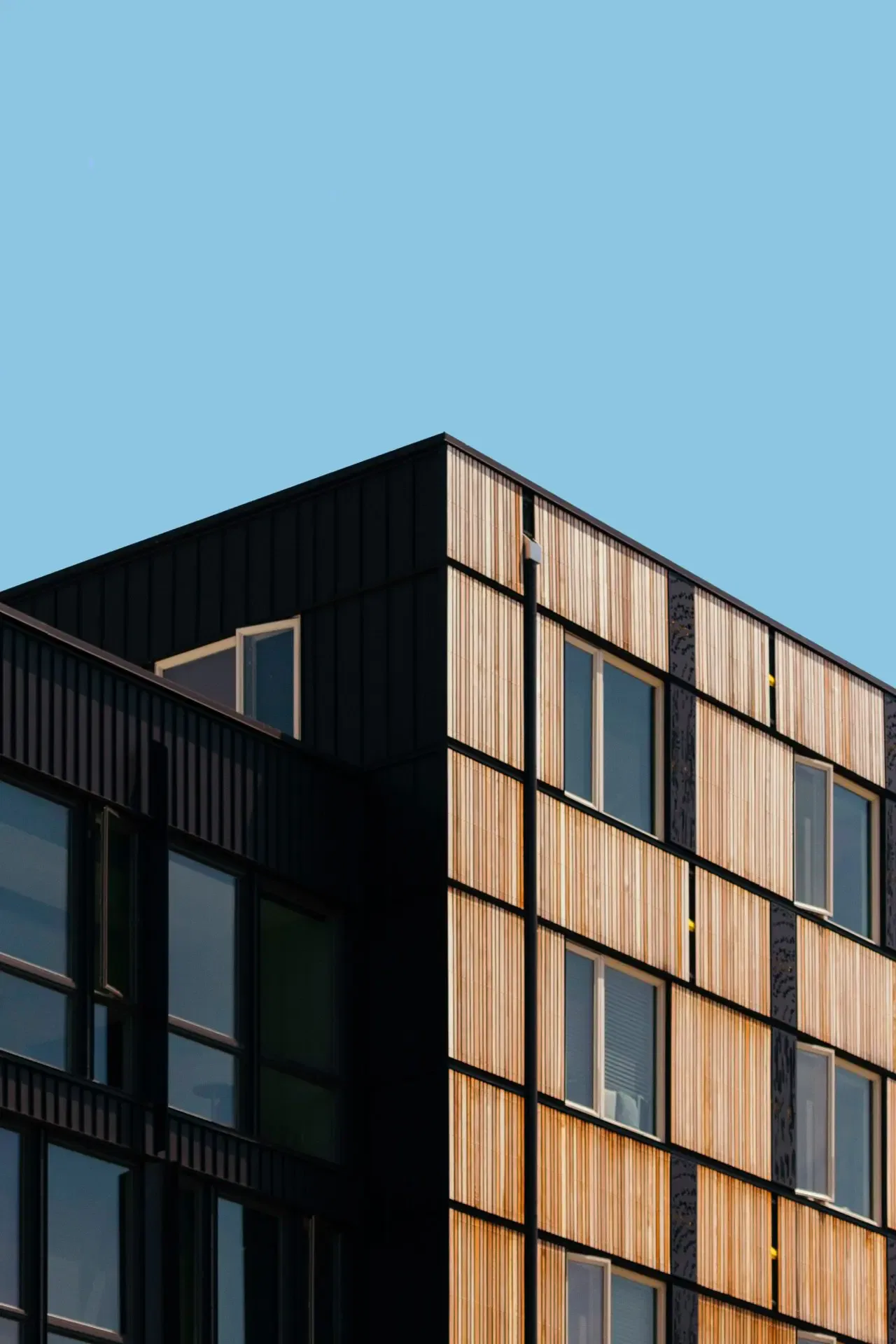 Modern building with a mix of black and wooden panels, featuring several windows, against a clear blue sky.