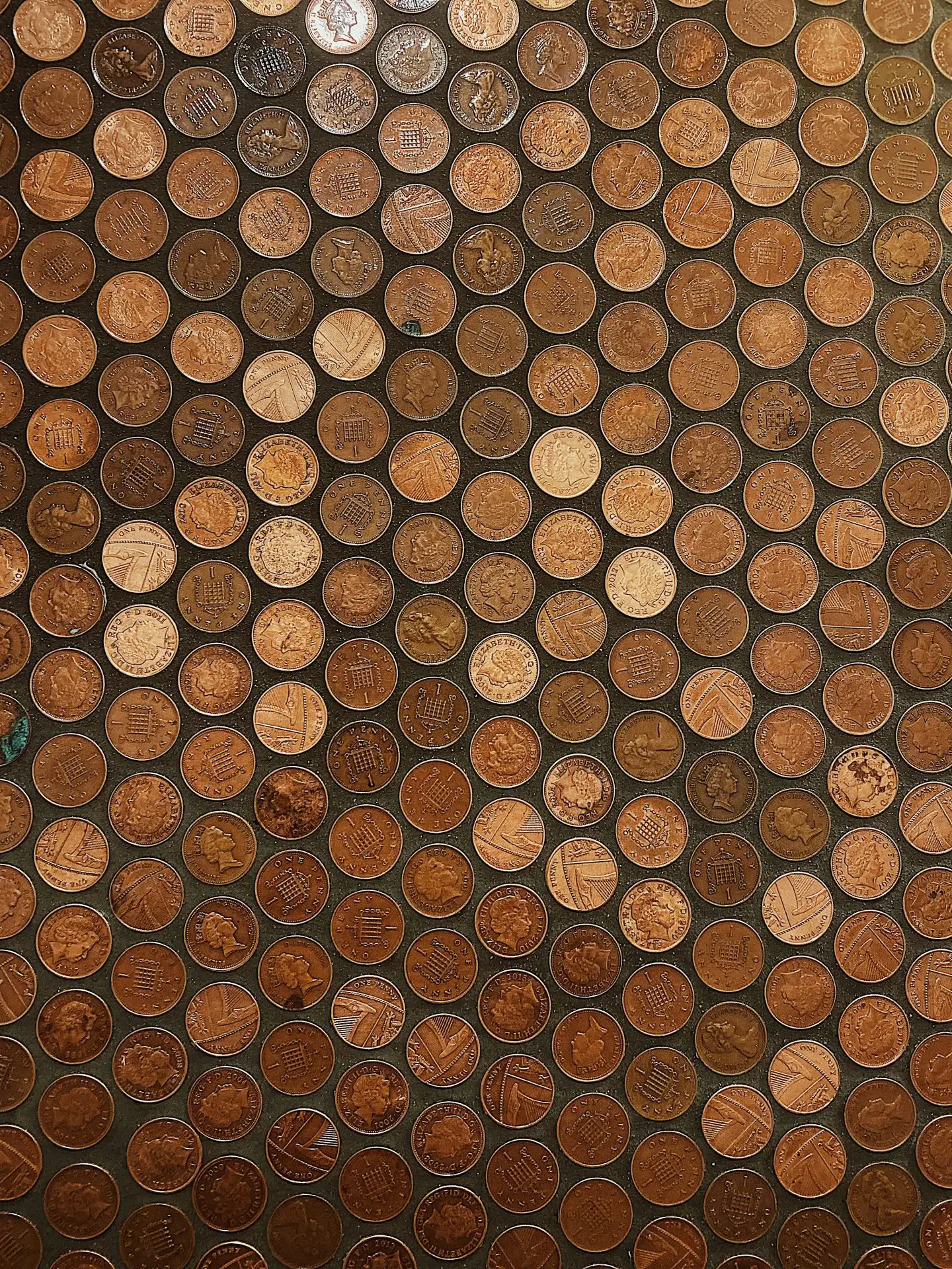 A wall covered with evenly spaced, weathered British pennies arranged in a grid pattern.