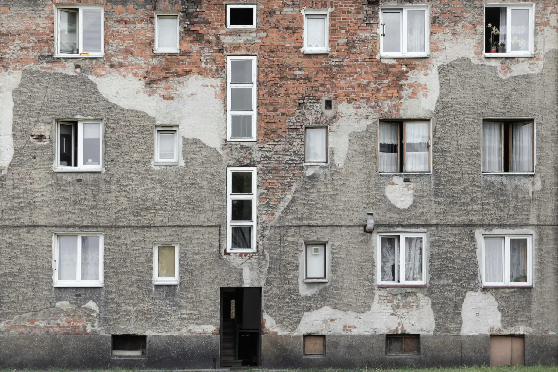 A weathered brick apartment building with visible patches of exposed brick and multiple windows in various conditions.