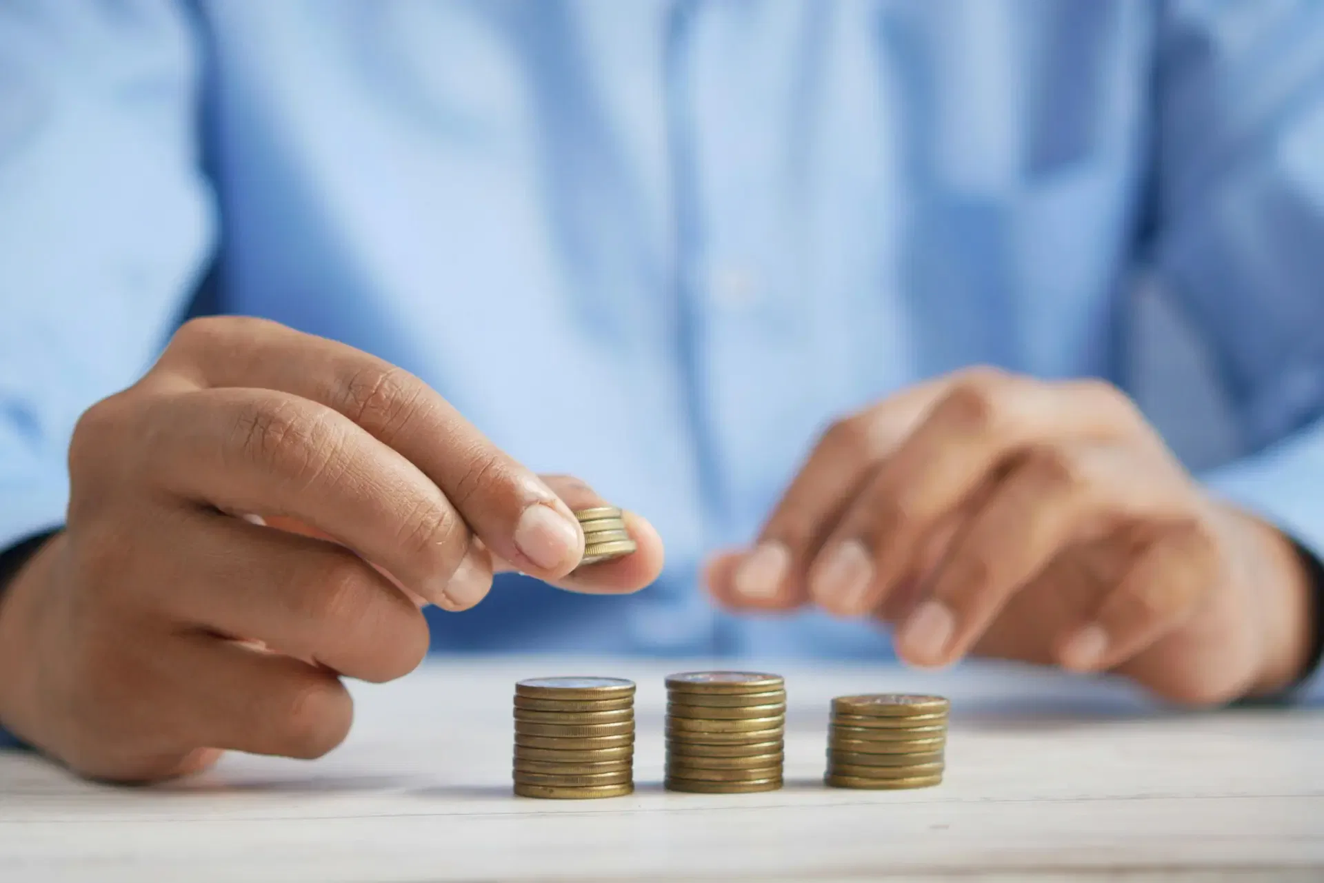 A person in a blue shirt stacks coins on a white table, with three piles of coins already formed.