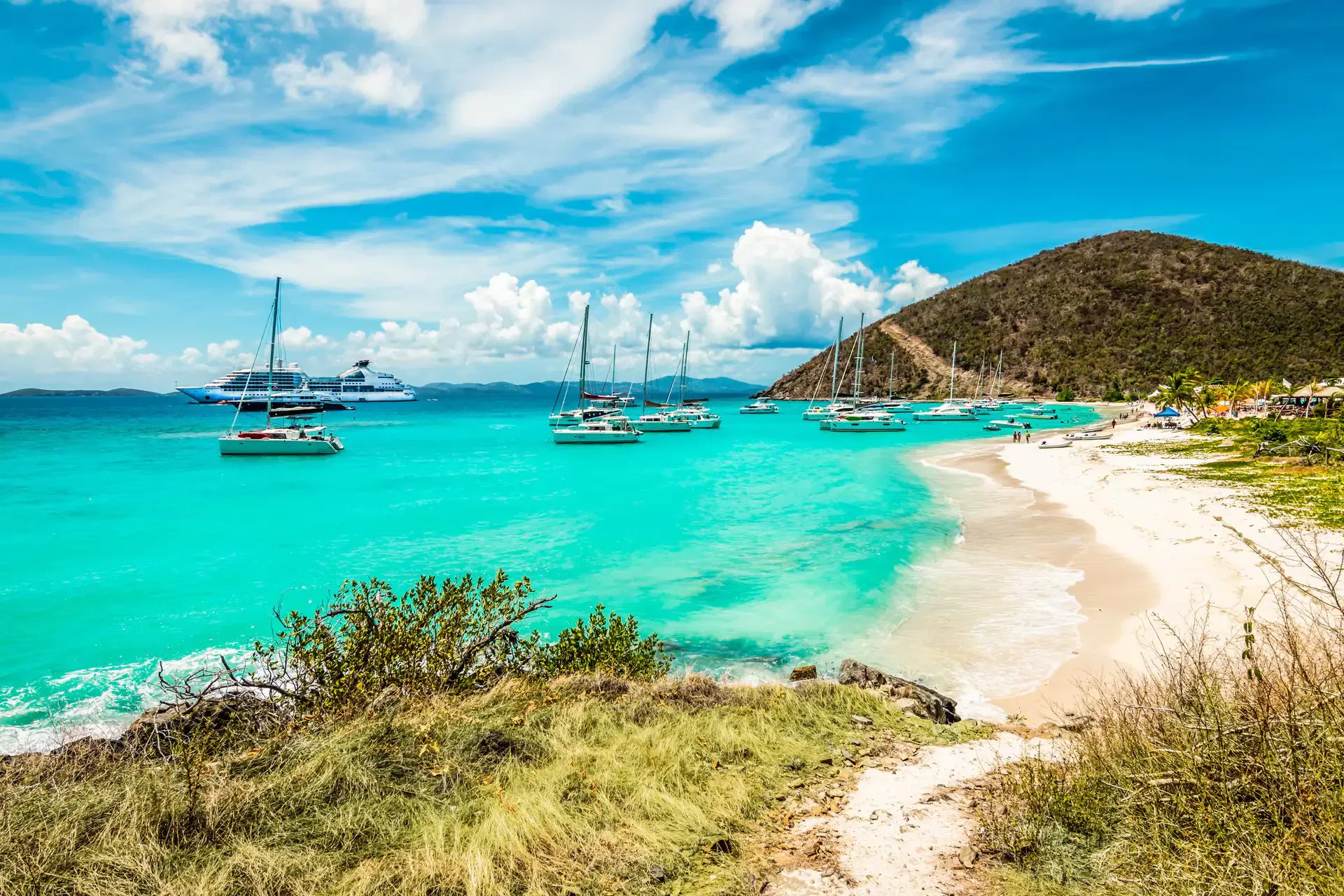 Luxury yachts anchored in turquoise waters near a pristine beach in the British Virgin Islands (BVI).