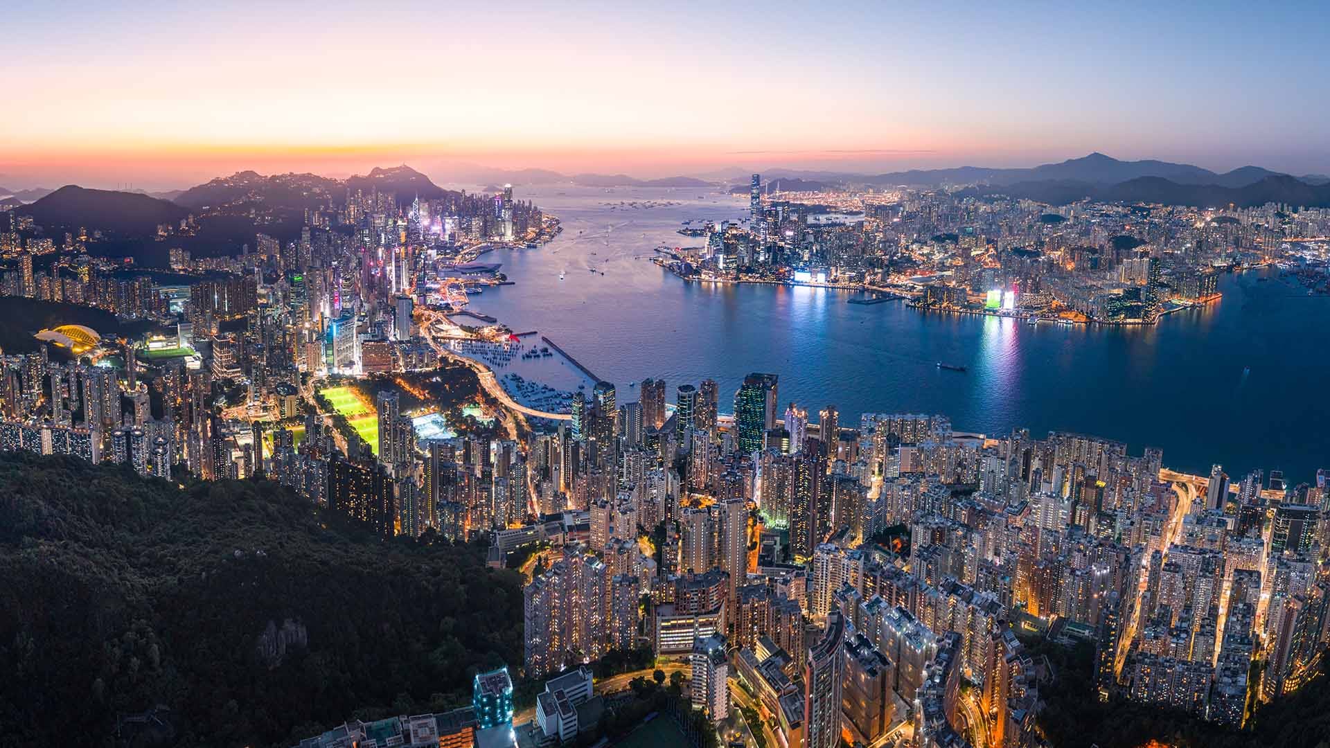 Aerial view of Hong Kong at night, showcasing the city's dense skyline and harbor.