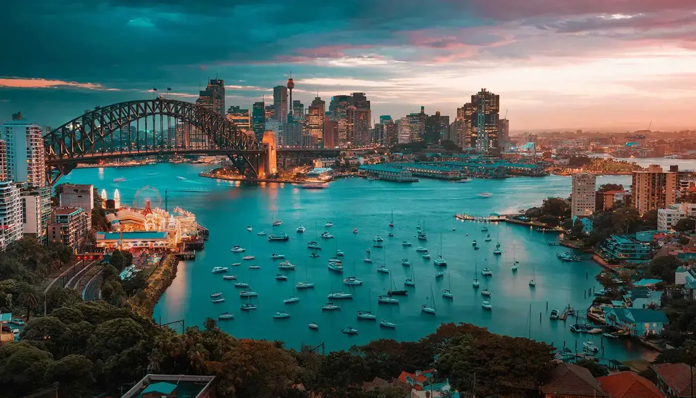 Sydney Harbour Bridge at sunset, with city skyline and boats.