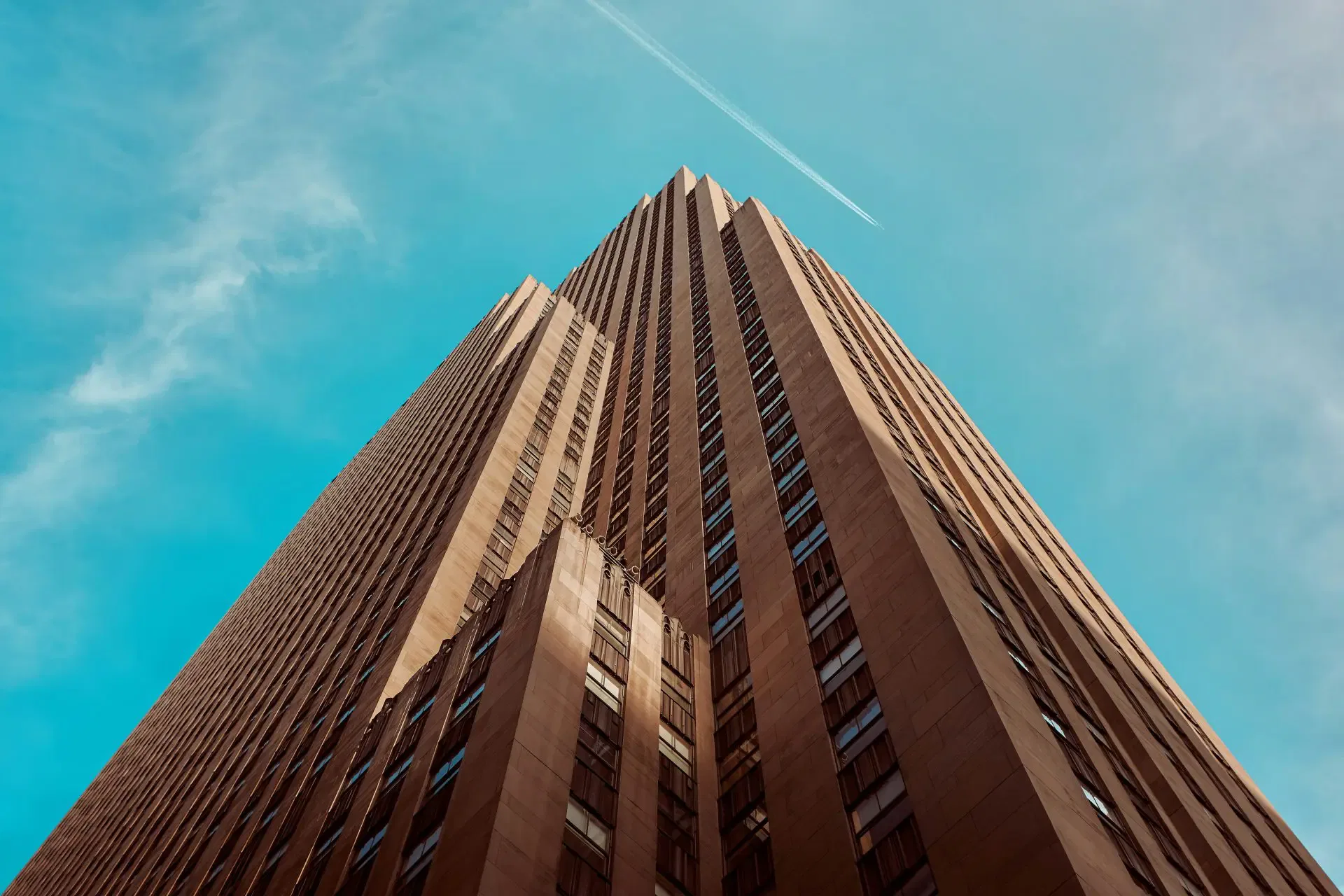 Low-angle view of a tall, brown skyscraper against a blue sky.