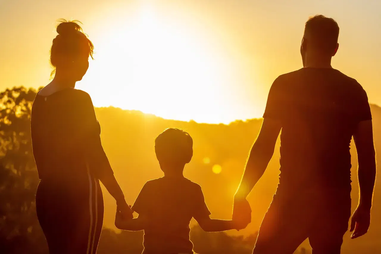 Silhouette of a family of three holding hands at sunset.