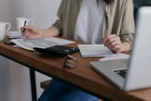 Person calculating 183-day test tax with documents, calculator, notebook, and laptop on a desk.