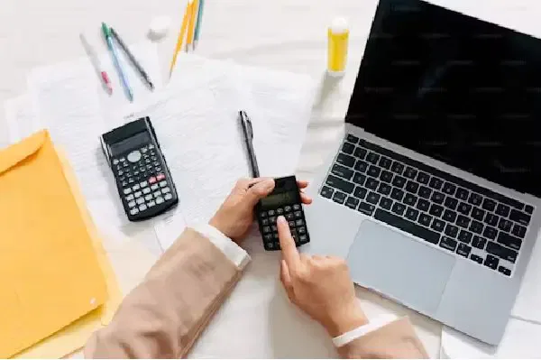 Person calculating domicile test tax with a laptop, papers, and two calculators on a desk.
