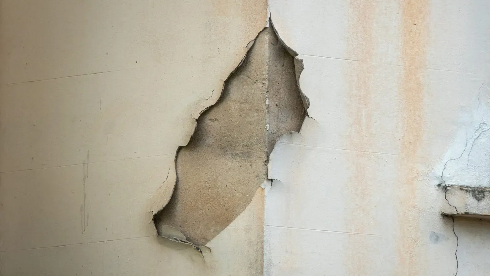 Cracked wall showing peeling plaster, highlighting building defects. Discussing who pays for building defects.