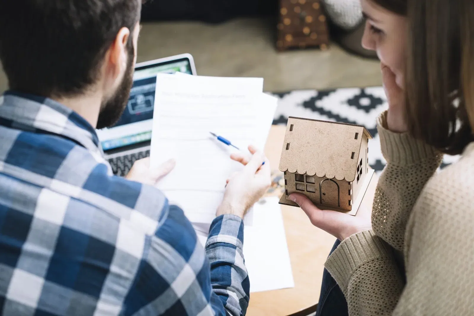 Couple reviewing estate planning documents with a laptop, holding a small house model; Lebanon international estate planning.