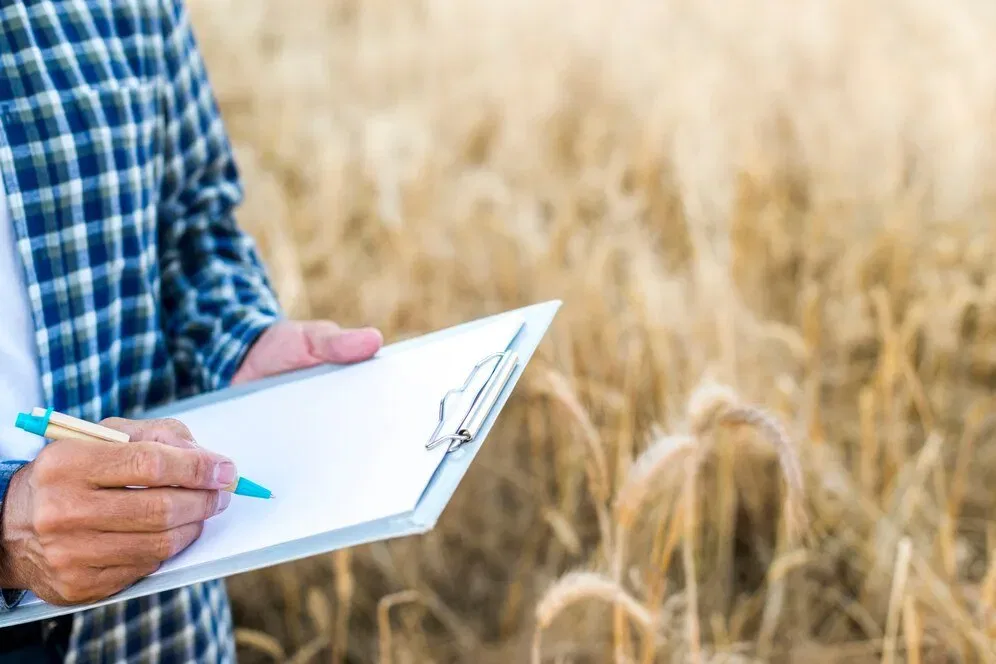 Farmer reviewing farm estate plan checklist on clipboard in wheat field.