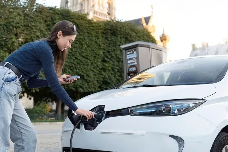 Woman charging electric vehicle at public charging station. NSW strata EV charging.