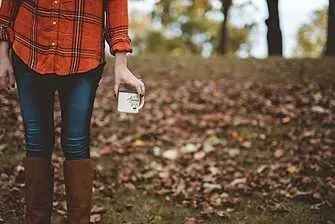 Woman in boots holding a coffee mug outdoors in autumn.