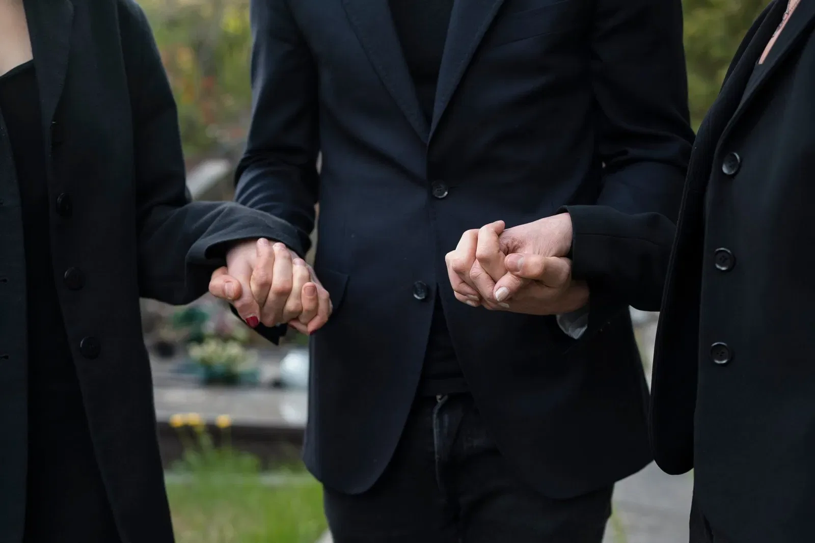 Three people in black mourning attire holding hands, symbolizing grief and support during the probate process after the death of an executor.