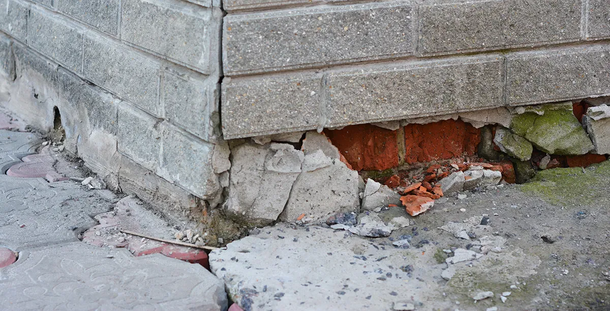Severe foundation damage at a building corner, showing cracked bricks and mortar. Strata building defect.