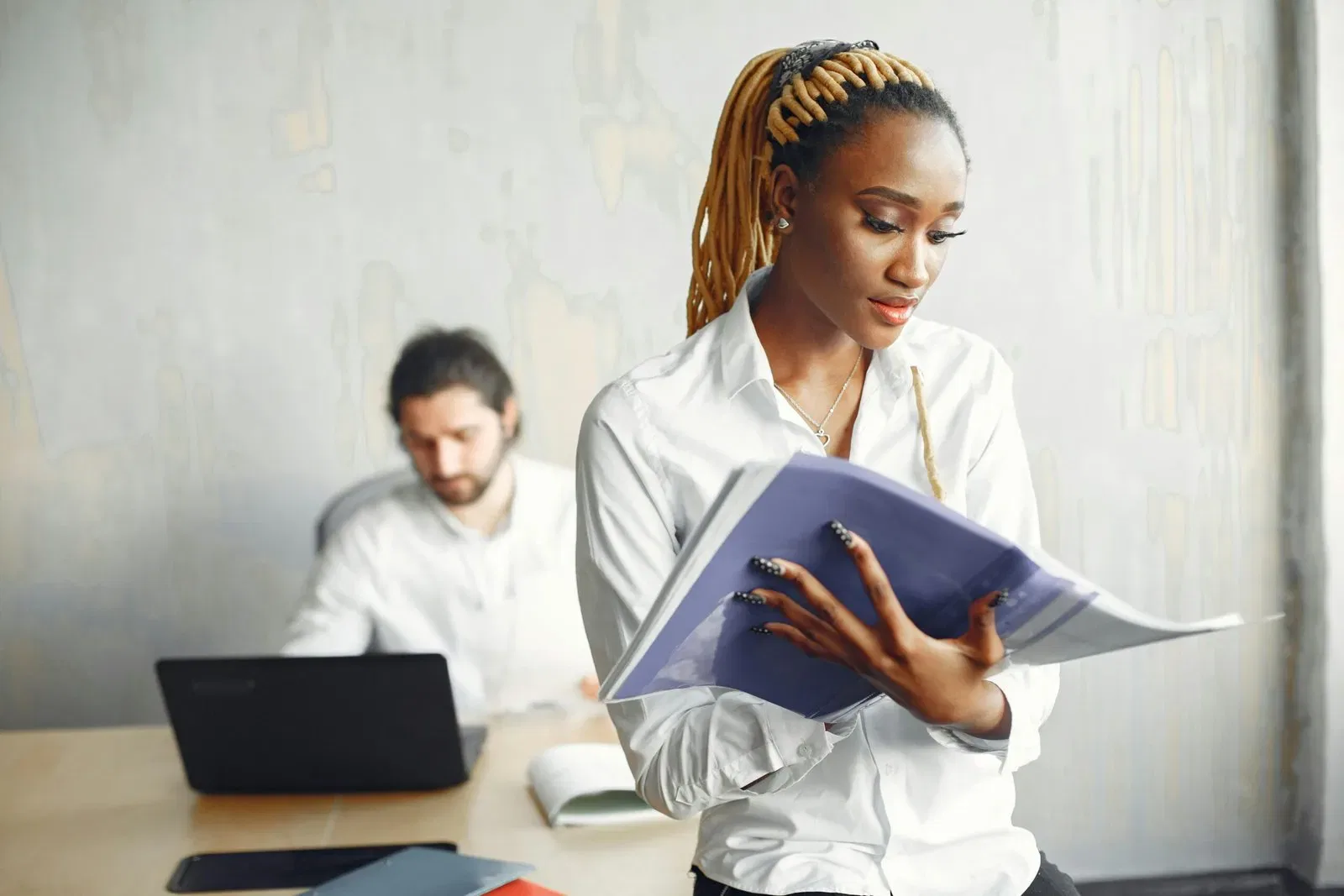 Businesswoman reviewing documents at her desk. A colleague works on a laptop in the background.