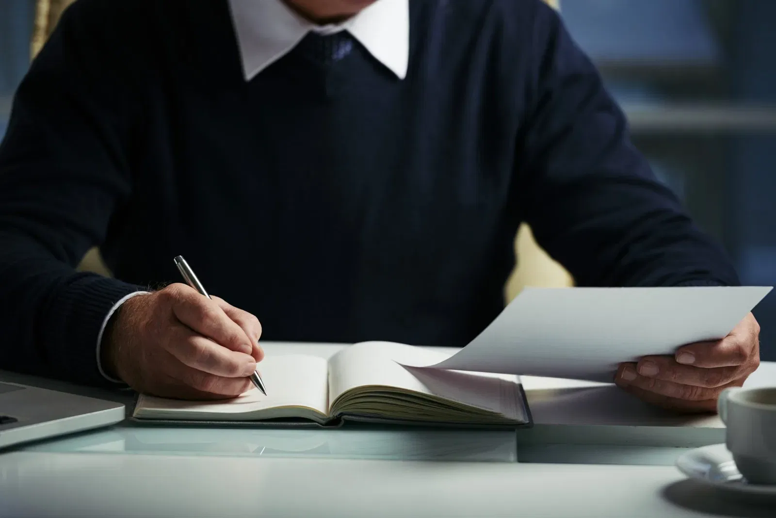 Person writing in a notebook at a desk with a laptop beside