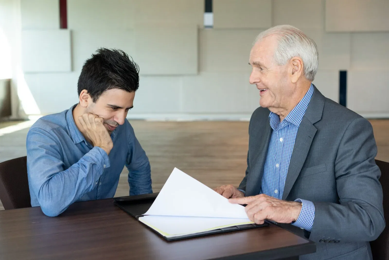 Two men discussing documents at a table in an office