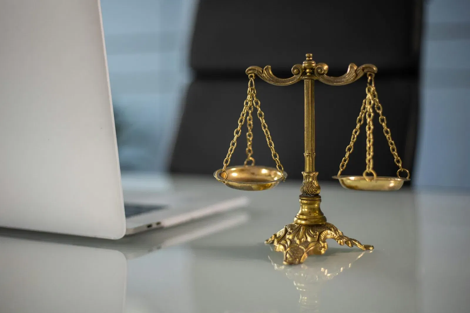 Brass scales of justice on a table near a laptop. Symbol of legal fairness.