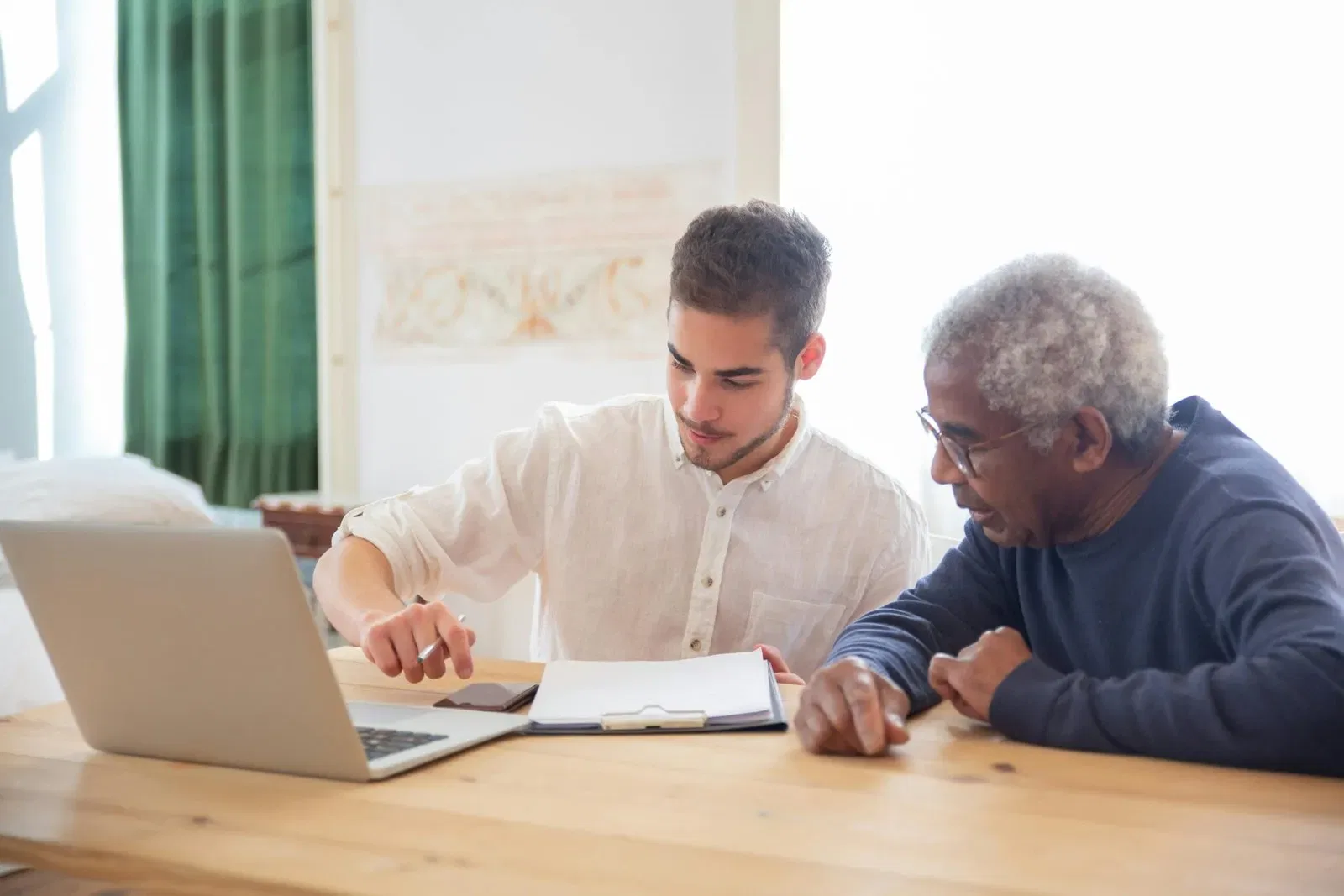 Young man and senior reviewing documents and laptop, discussing estate planning options for a will.