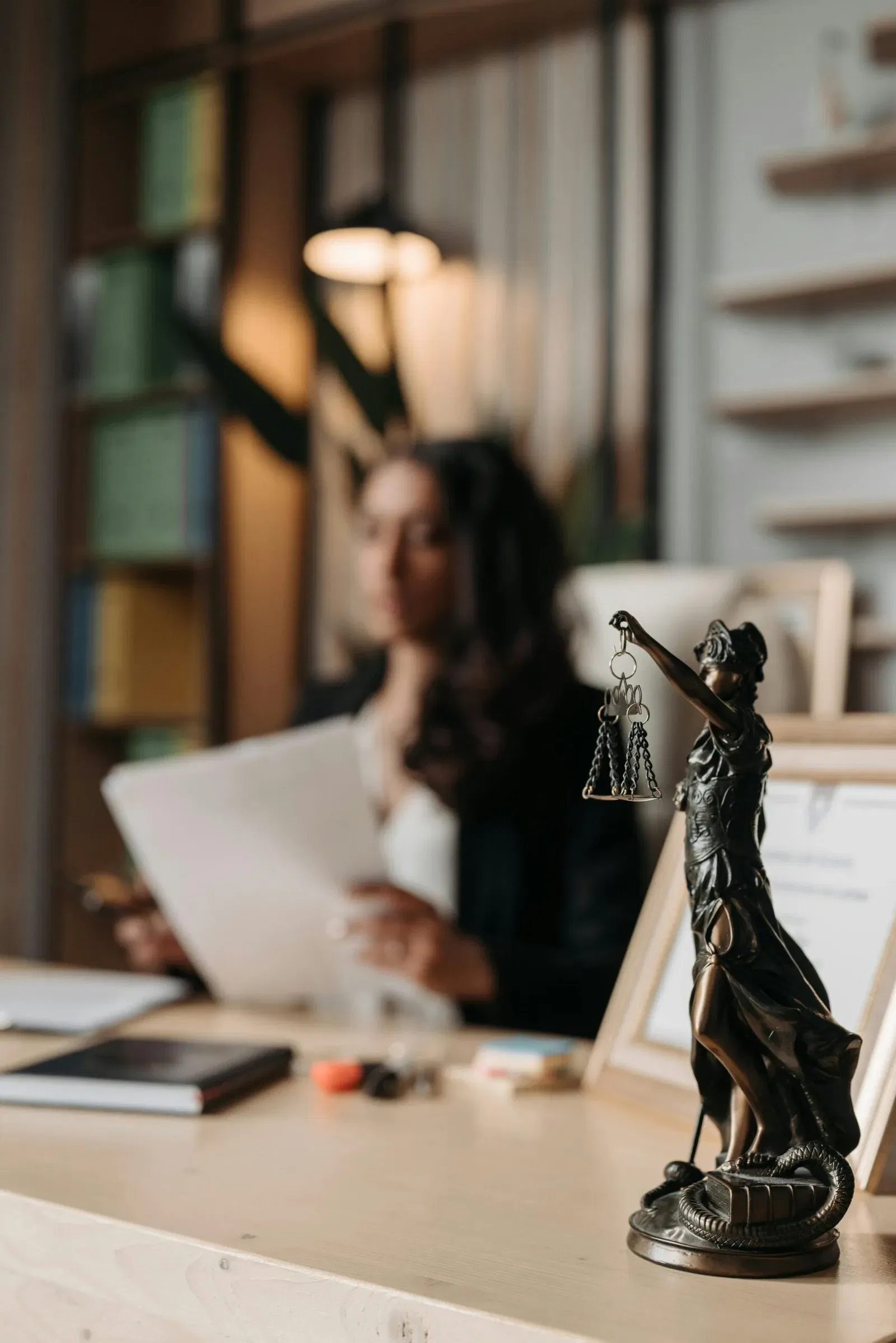 Lady Justice statue on a desk, with a lawyer reviewing documents in the background.