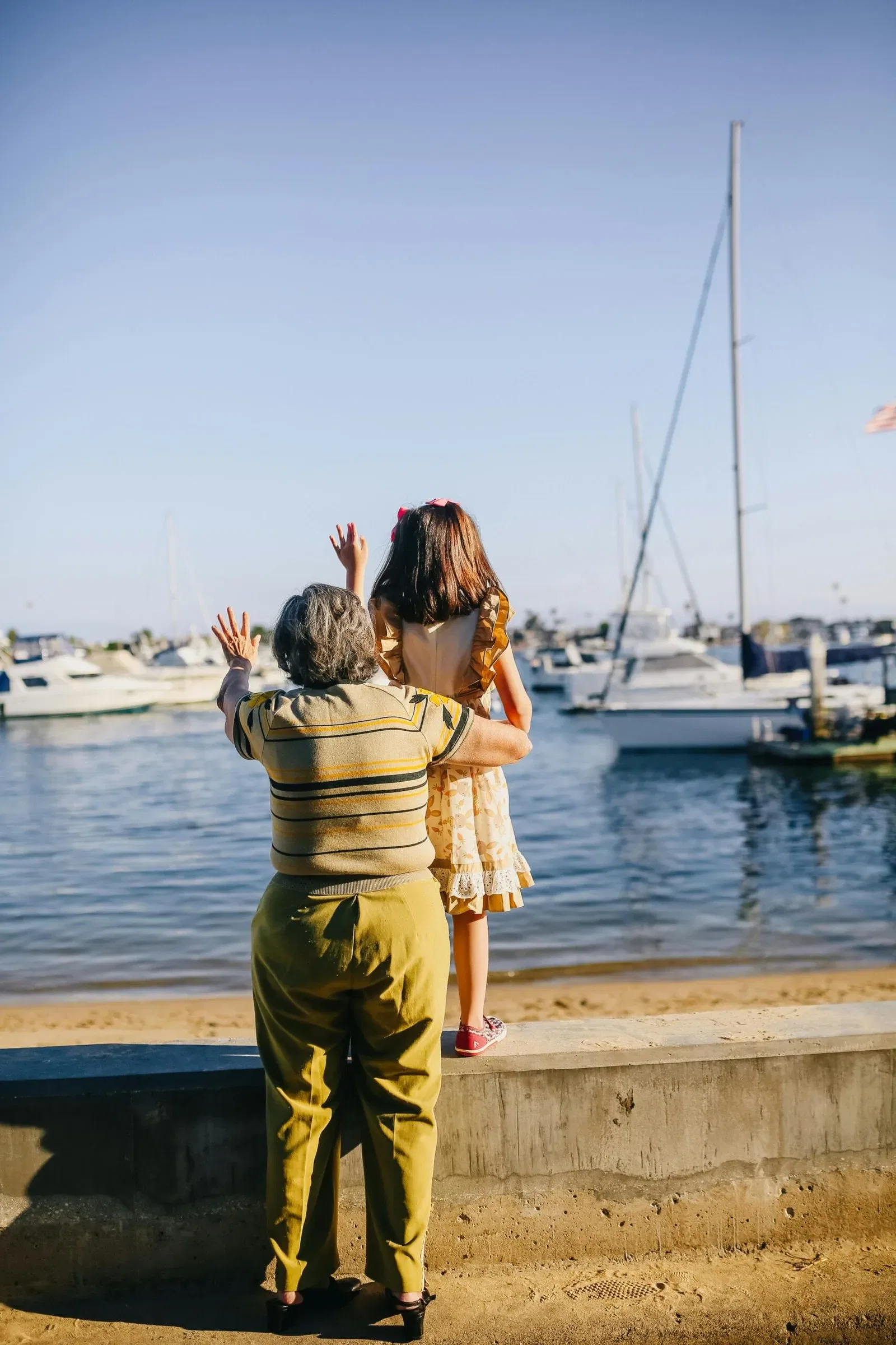 Woman and girl look at boats, raising arms.