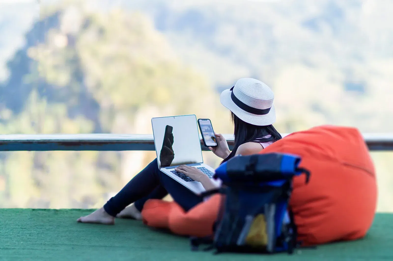 Influencer working remotely with laptop and phone, backpack nearby. Mountain view backdrop.