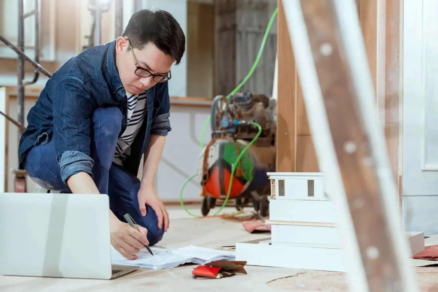 Architect reviewing blueprints and a building model on a construction site.