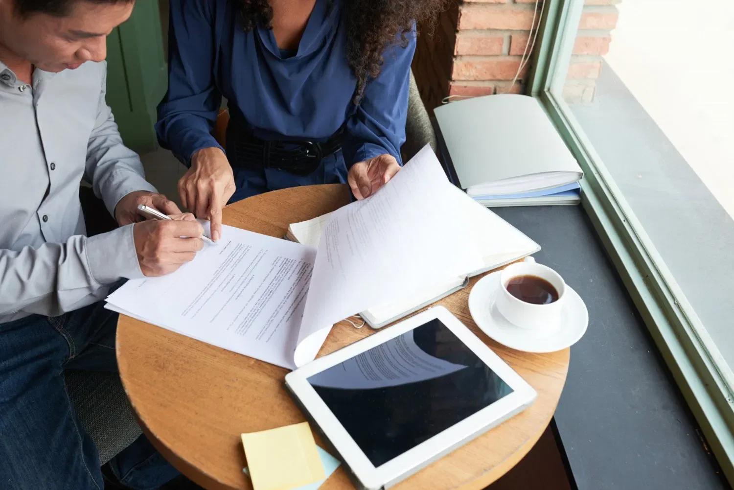 Two people reviewing estate plan documents at a table with a tablet and coffee.