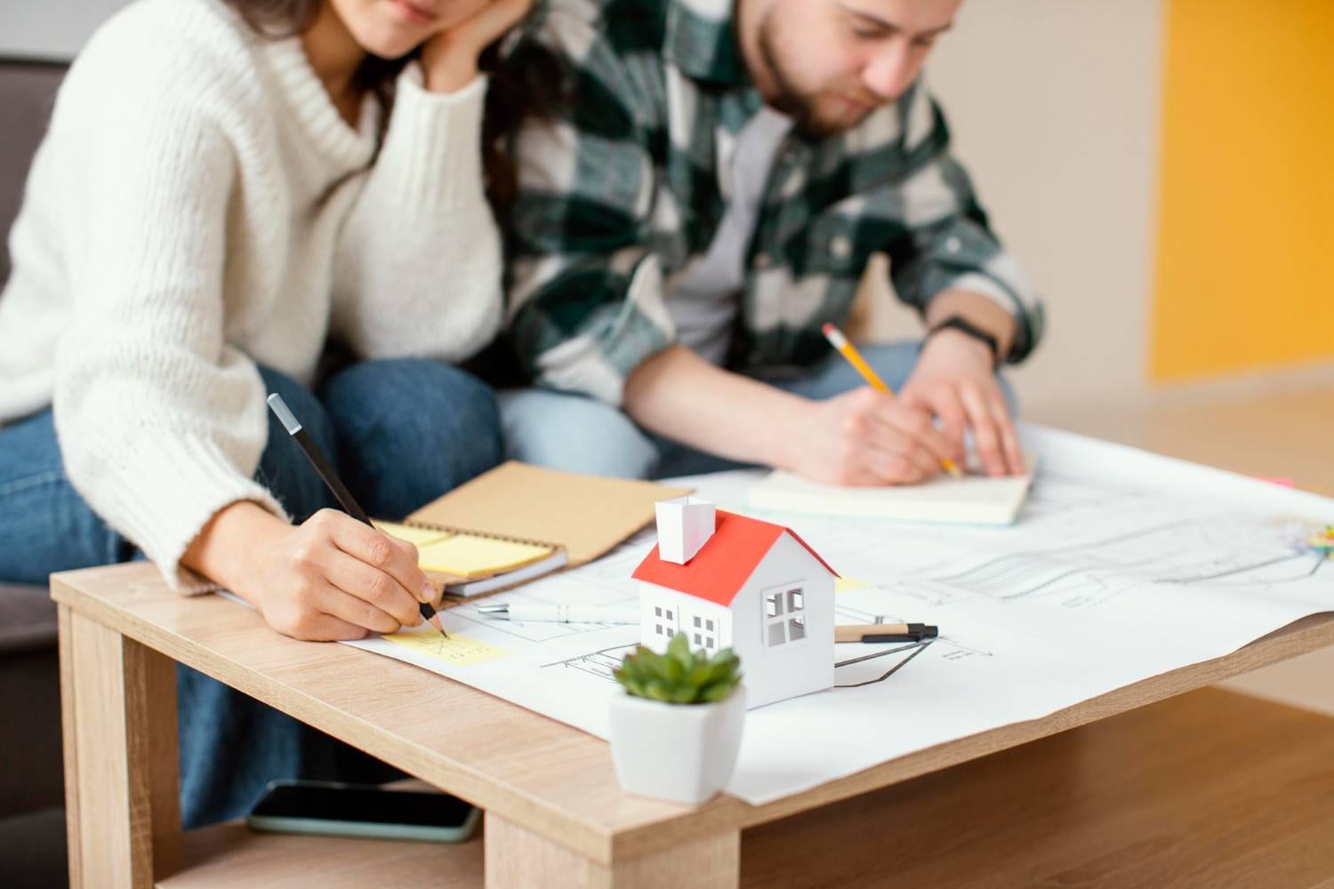 Couple planning a new home with blueprints and a model house on the table.